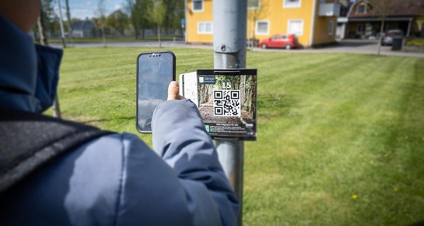Pojke scannar QR-kod för X-rundan på en lyktstolp med sin telefon. 